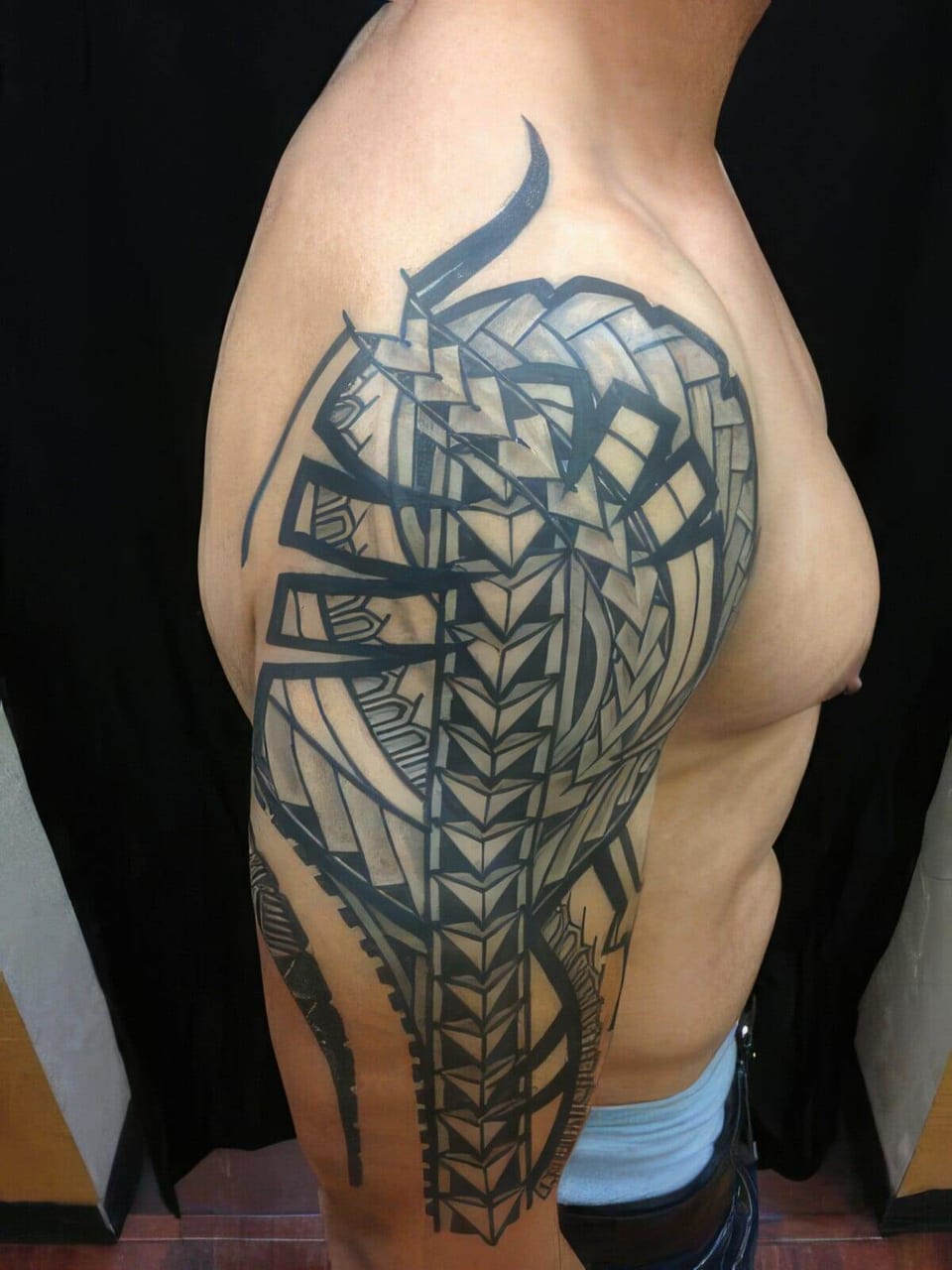 Large black Polynesian-style tribal tattoo with woven panels covering a shoulder and upper arm, tattooed by Seth Reynolds