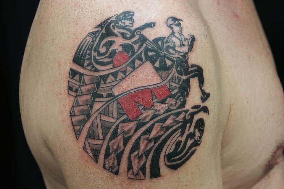 Round Polynesian-style tattoo with a runner, a wrestler and red accents on a shoulder, tattooed by Seth Reynolds