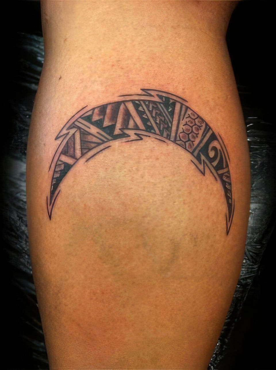 Black crescent-shaped Polynesian-style band with chevrons tattooed on a calf, tattooed by Seth Reynolds