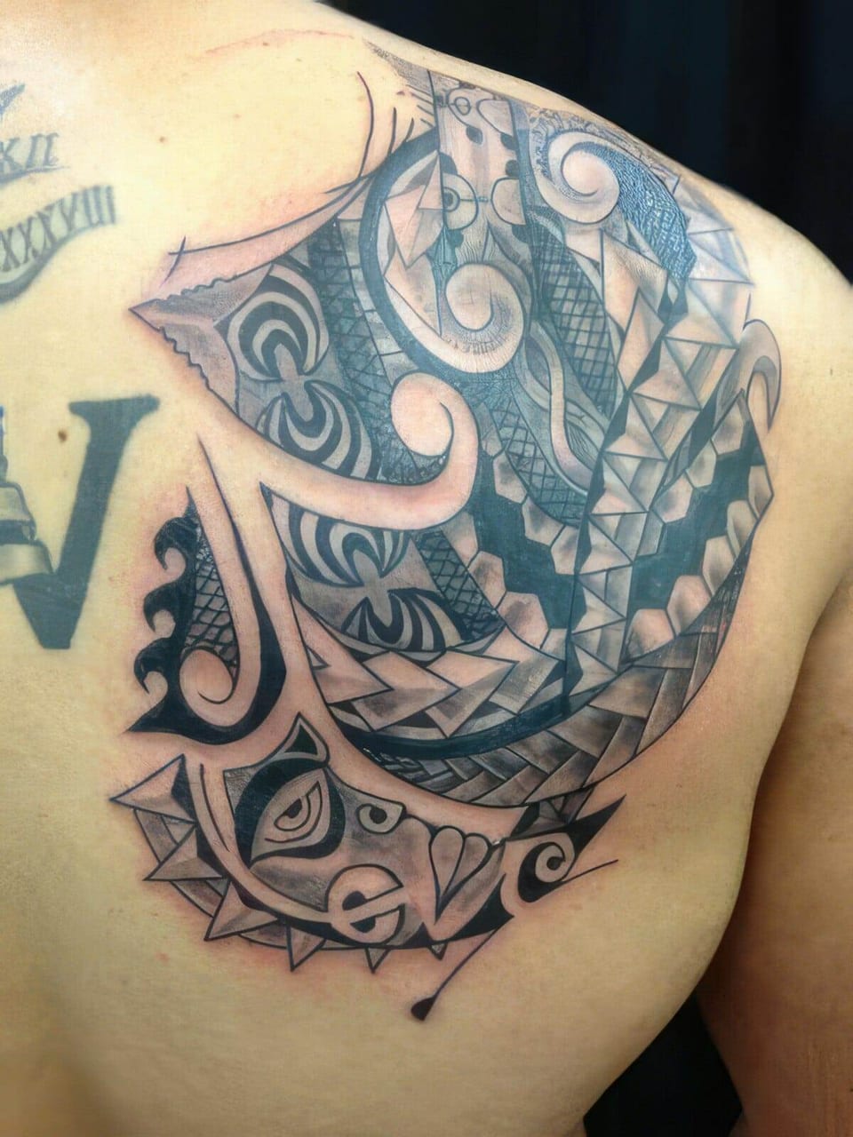 Black Polynesian-style spiral and wave pattern with blue-gray shading tattooed on a shoulder blade, tattooed by Seth Reynolds