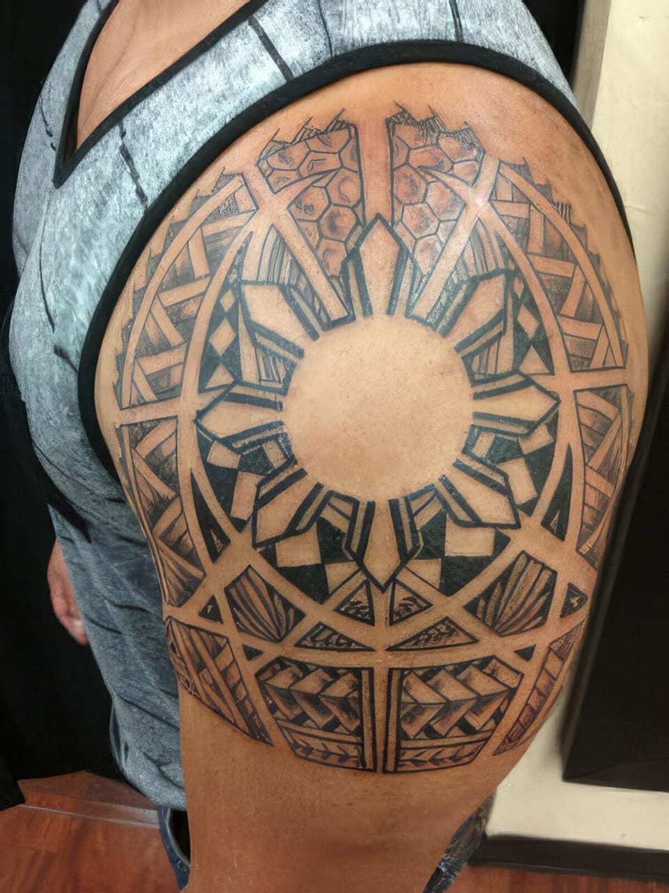 Black Polynesian-style sun pattern with radiating panels tattooed on a shoulder, tattooed by Seth Reynolds
