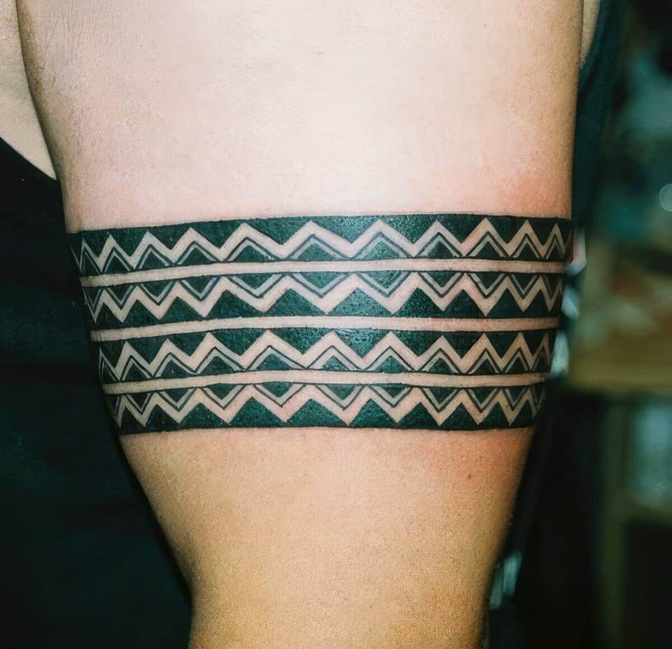 Black tribal armband with white zigzag triangle patterns tattooed around an upper arm, tattooed by Seth Reynolds
