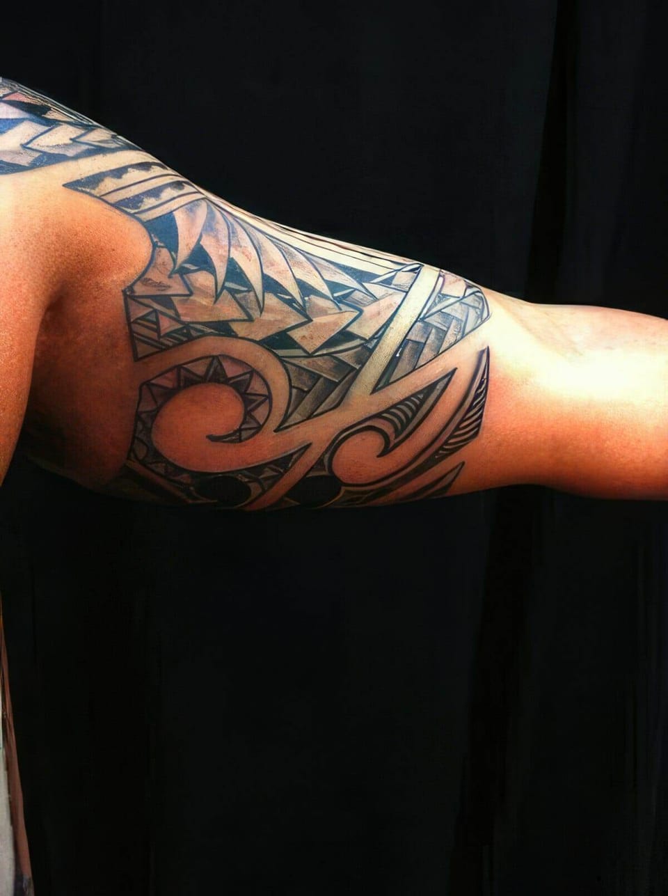 Black Polynesian-style spiral pattern tattooed around a shoulder and upper arm, tattooed by Seth Reynolds