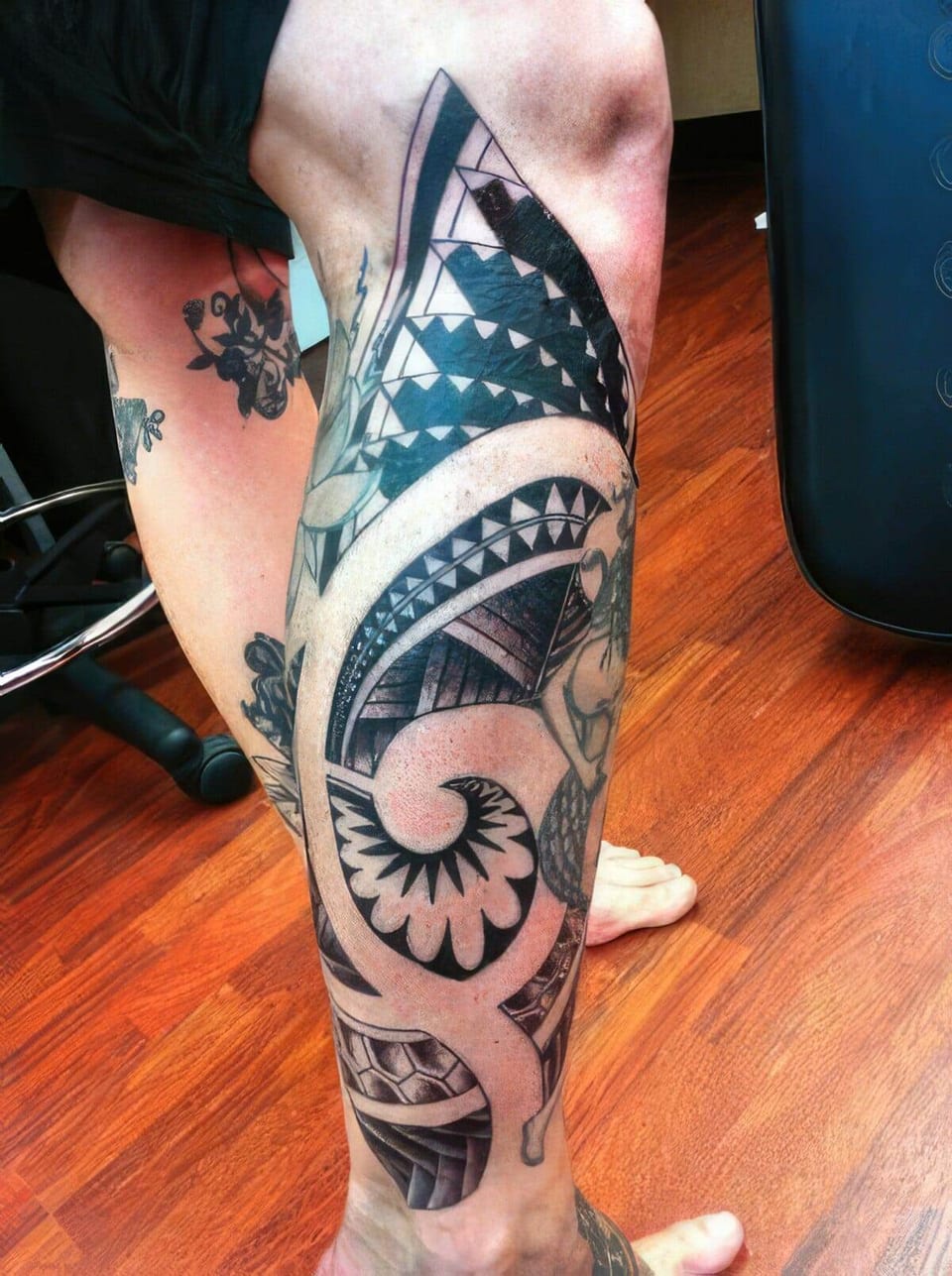 Black Polynesian-style spiral pattern tattooed down a calf, seen from behind, tattooed by Seth Reynolds