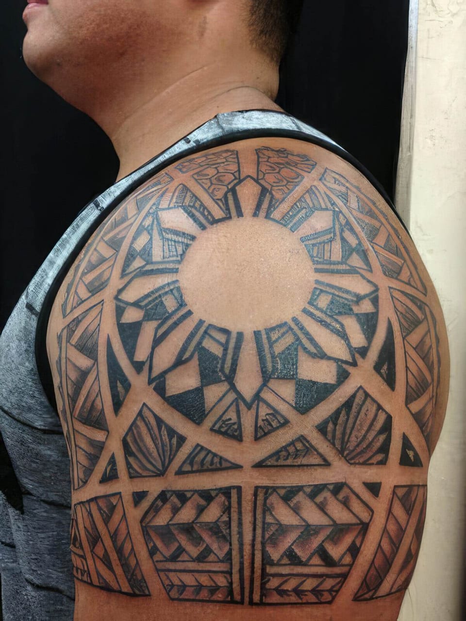 Black Polynesian-style sun pattern with radiating panels tattooed on a shoulder, seen from the side, tattooed by Seth Reynolds