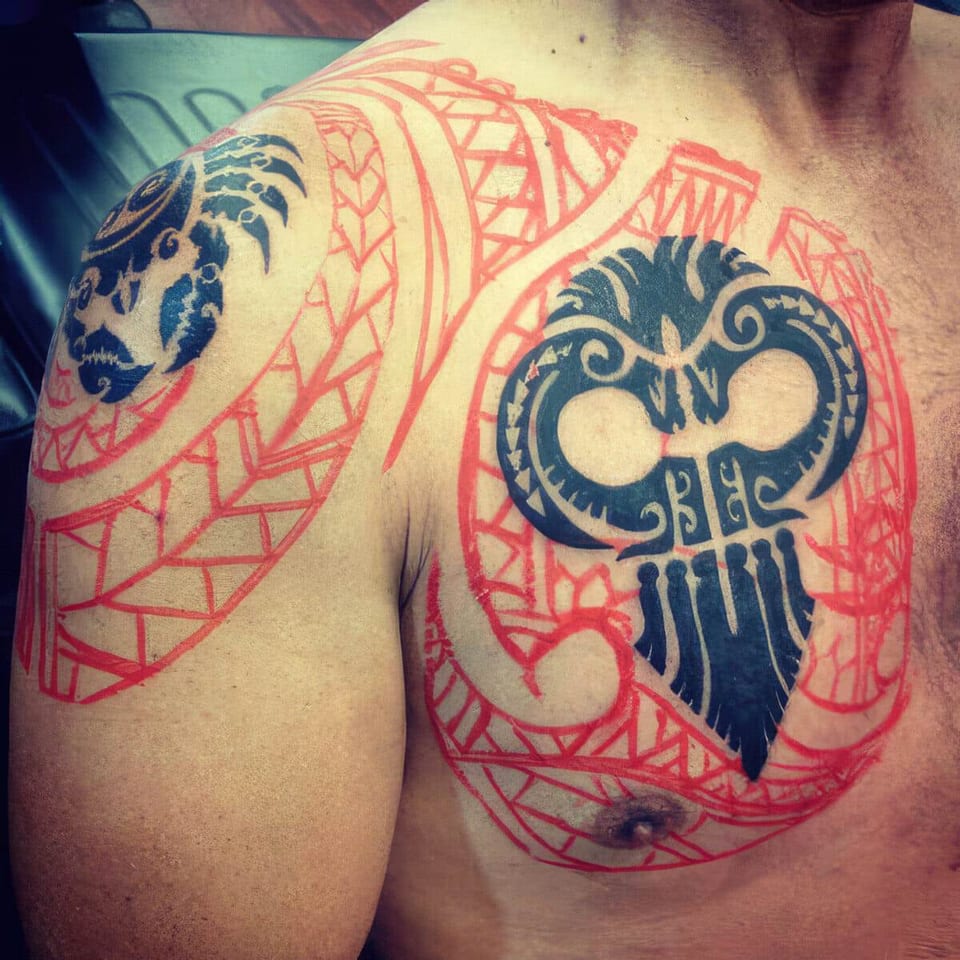 Red-outlined tribal stencils with a blue and black owl mask on a chest and shoulder, tattooed by Seth Reynolds