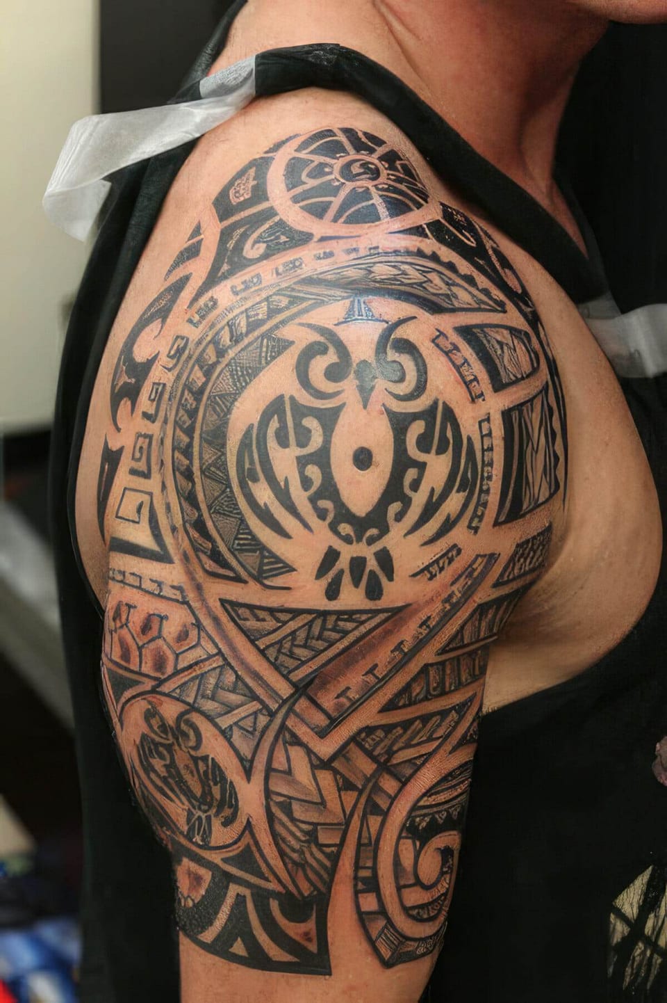 Black Polynesian-style owl and spiral pattern tattooed on a shoulder and upper arm, tattooed by Seth Reynolds