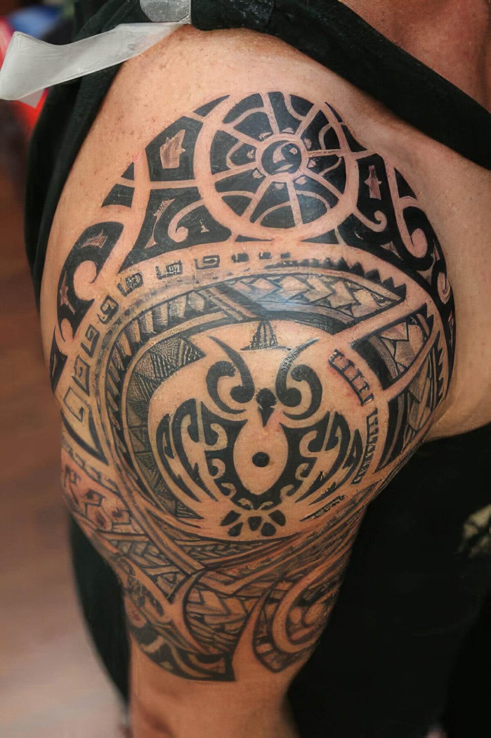 Black Polynesian-style sun and owl pattern tattooed on a shoulder and upper arm, tattooed by Seth Reynolds