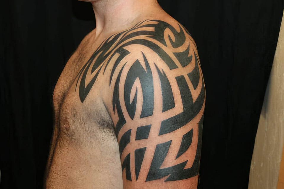 Black tribal tattoo with bold curved bands covering a shoulder and upper arm, tattooed by Seth Reynolds