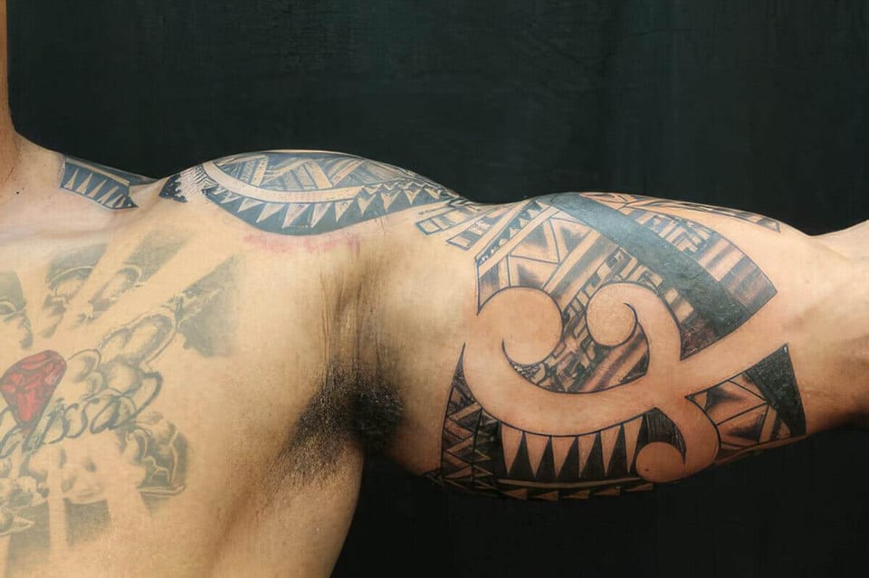 Black Polynesian-style spiral and wave pattern tattooed on an upper arm, tattooed by Seth Reynolds