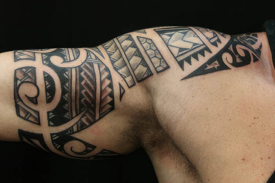 Black Polynesian-style musical notes and spirals tattooed on an upper arm, tattooed by Seth Reynolds