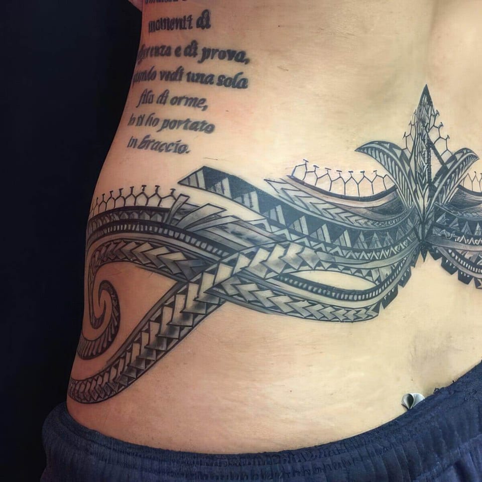 Black Polynesian-style tribal band across a lower back and hip, with script lettering above, tattooed by Seth Reynolds