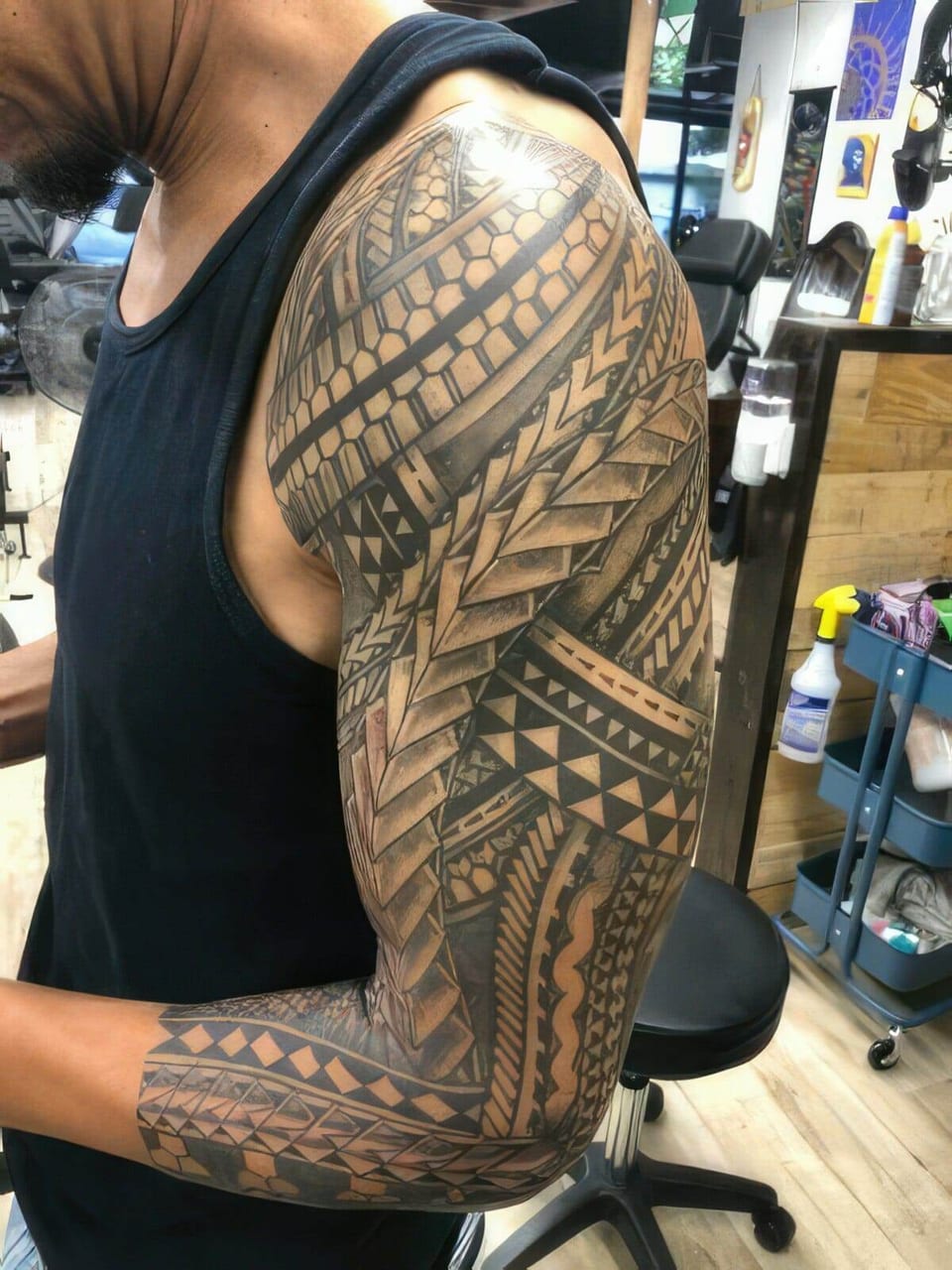 Black Polynesian-style full sleeve with chevron panels on a man in a black tank top, tattooed by Seth Reynolds