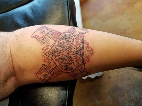 Black ornamental crossed nails sit on the forearm near the elbow over a red guide drawing.