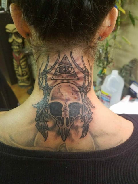 A black and grey illustrative bird skull, feathers and an eye in a triangle cover the back of the neck.