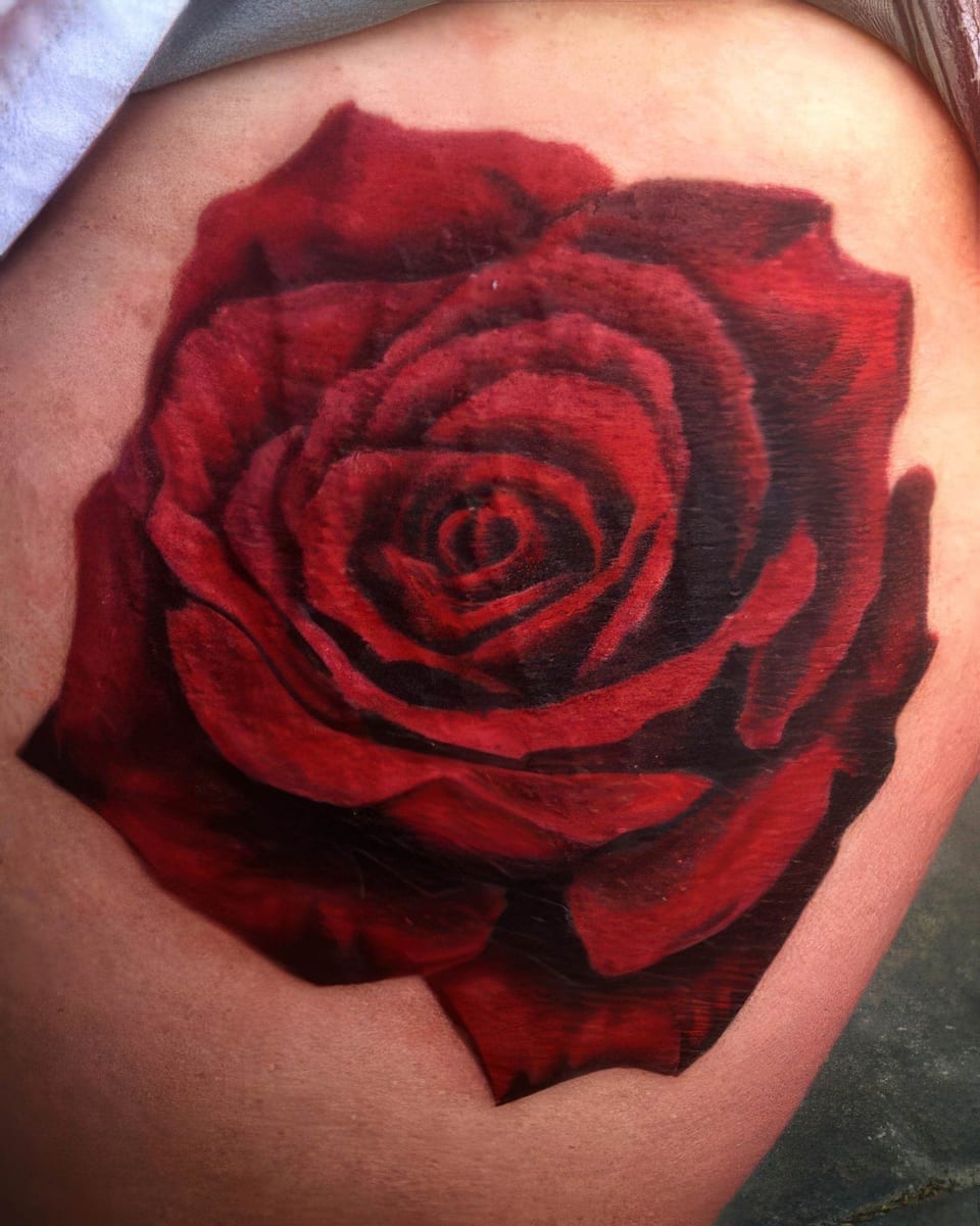 A realistic red rose with layered petals covers an upper arm.