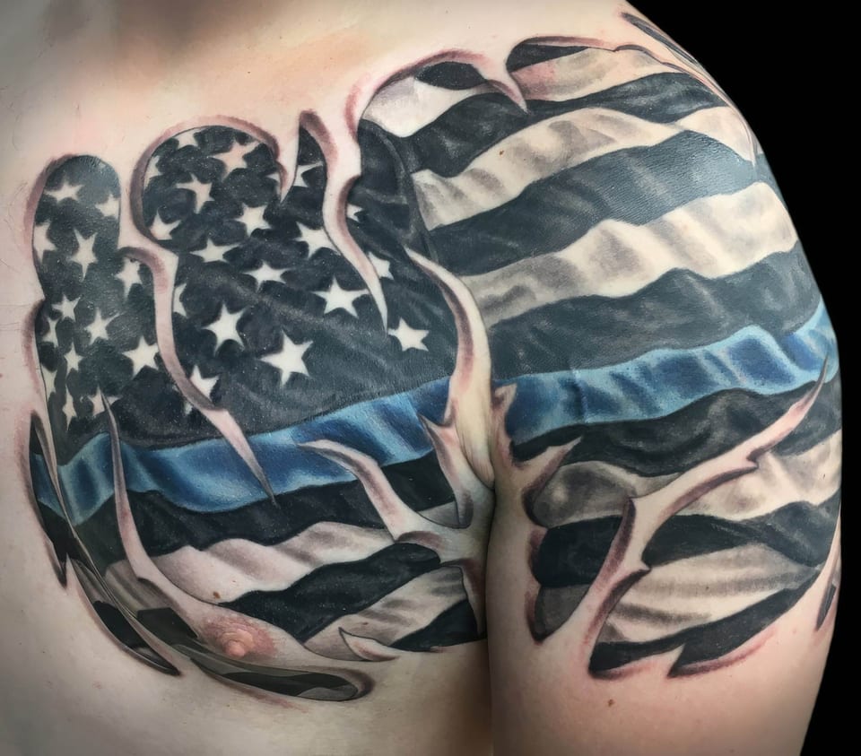 A realistic black and grey American flag with a blue stripe covers an upper chest and shoulder.