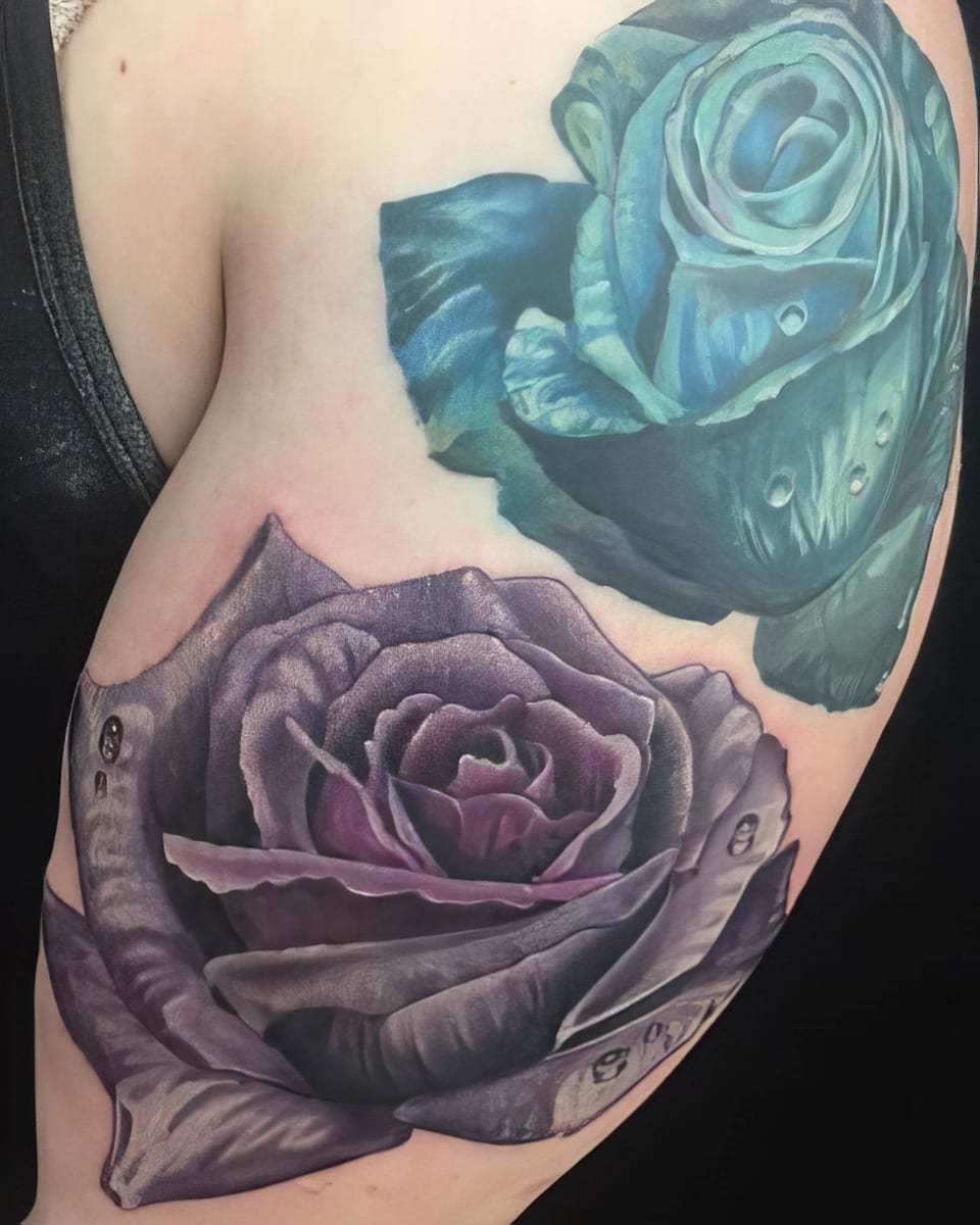 A realistic teal rose above a purple rose, both with water droplets, covers the upper arm.