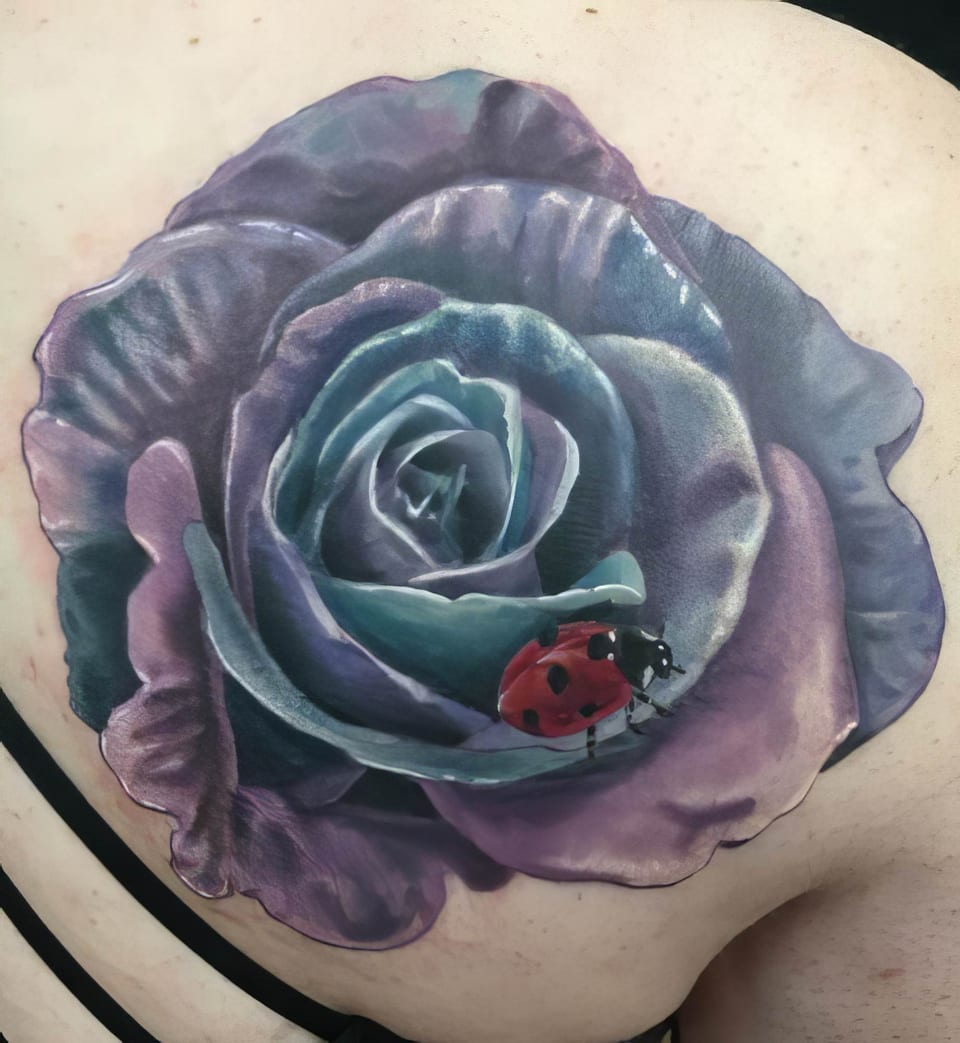 A realistic purple rose tattoo with a red ladybug on a petal covers a shoulder blade.