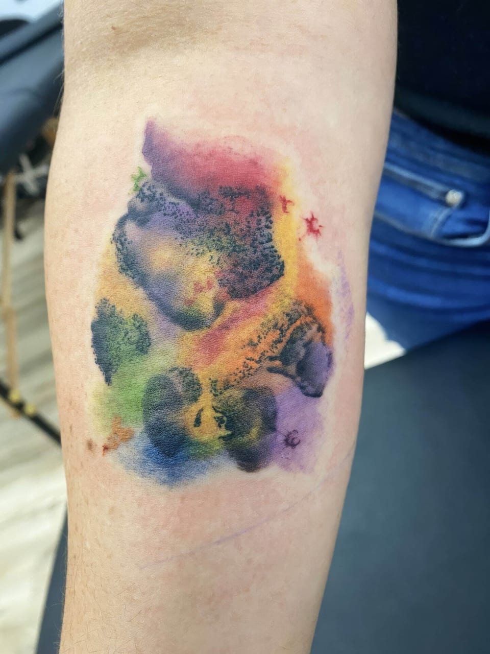 Black paw prints amid purple, yellow, red and green watercolor cover a forearm.