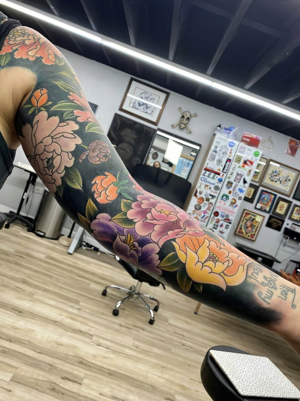 A color Japanese floral sleeve with peonies and green leaves covers an arm.