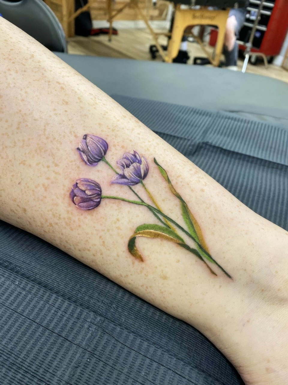 Realistic purple tulips with green stems and leaves cover a forearm.