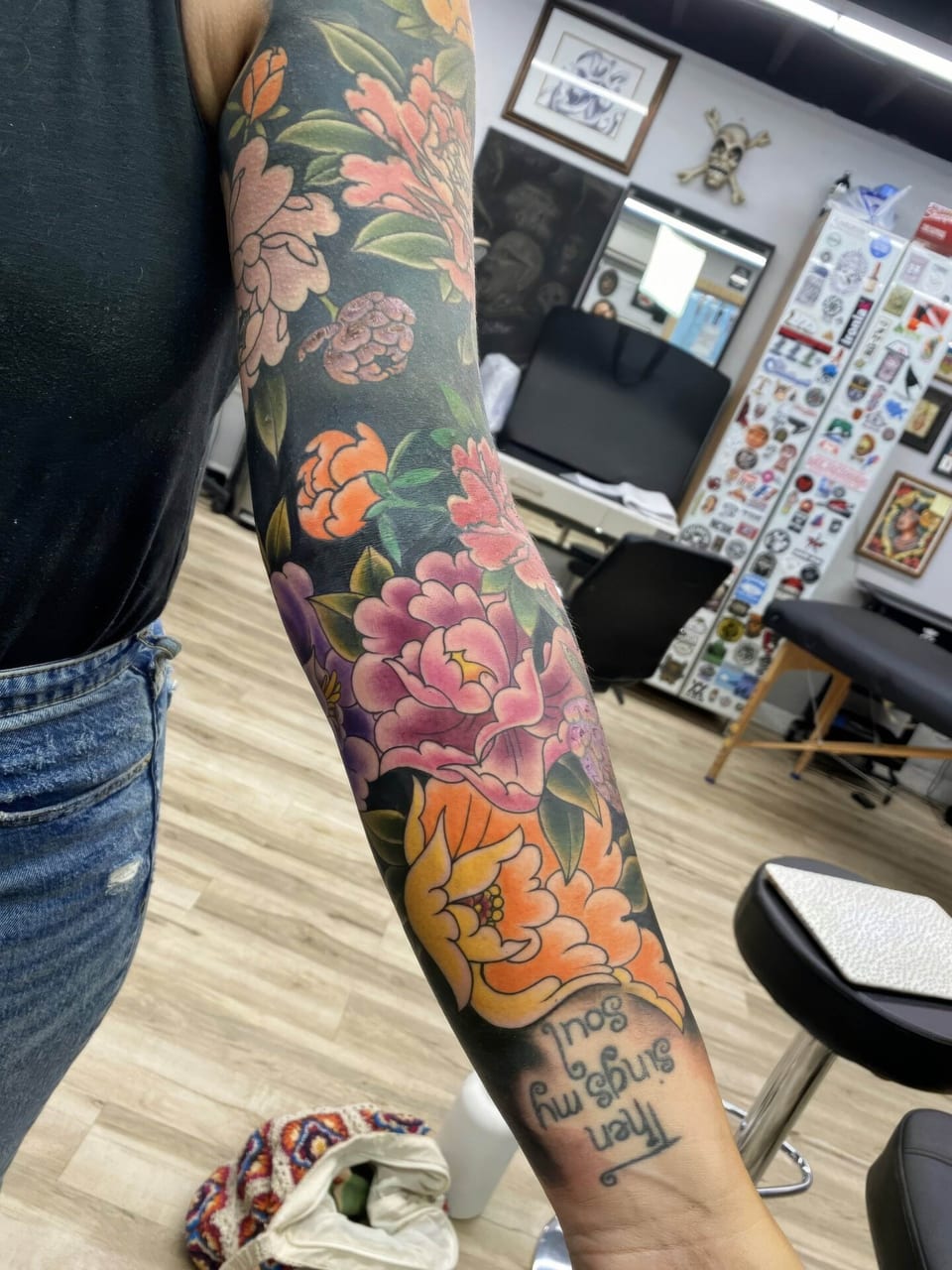 A color Japanese floral sleeve with peonies, green leaves and wrist lettering covers an arm.