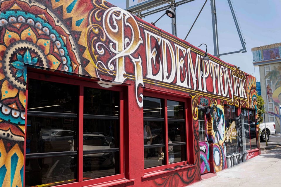 Redemption Ink's mural-covered storefront displays large white lettering above red-framed windows.