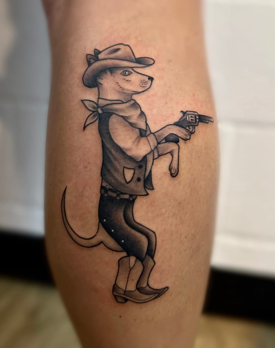 A black and grey illustrative cowboy dog in a hat, vest and boots holds a revolver on a calf.