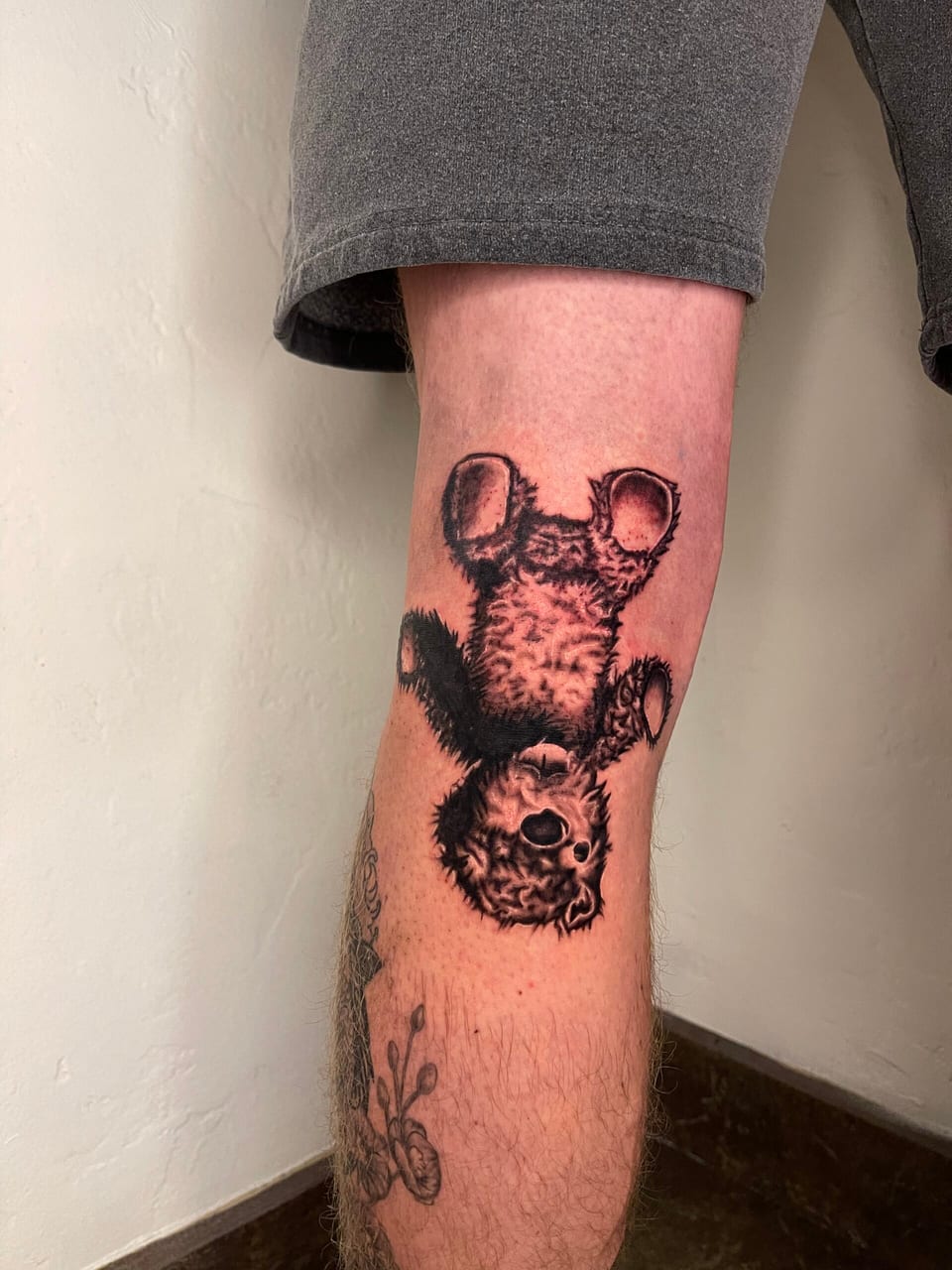 A black and grey illustrative upside-down bear sits on the thigh beneath shorts.