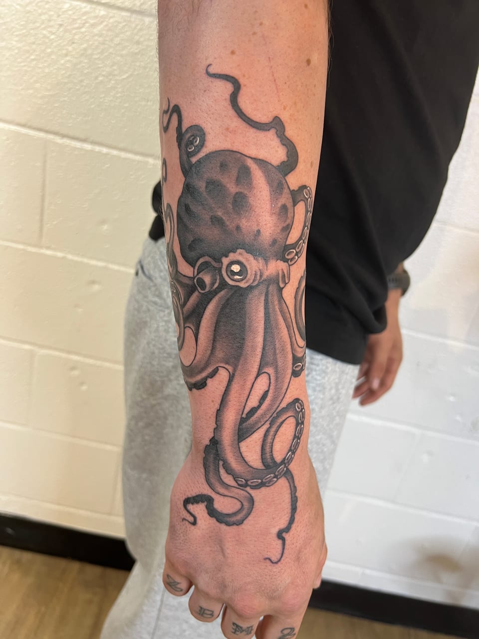 A black and grey illustrative octopus spreads curling tentacles down a forearm and onto the hand.