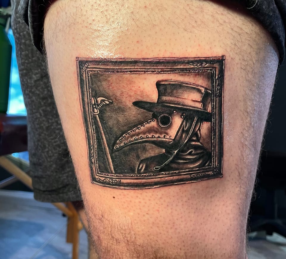 A black and grey realistic plague doctor in a top hat appears inside an ornate frame on a thigh.