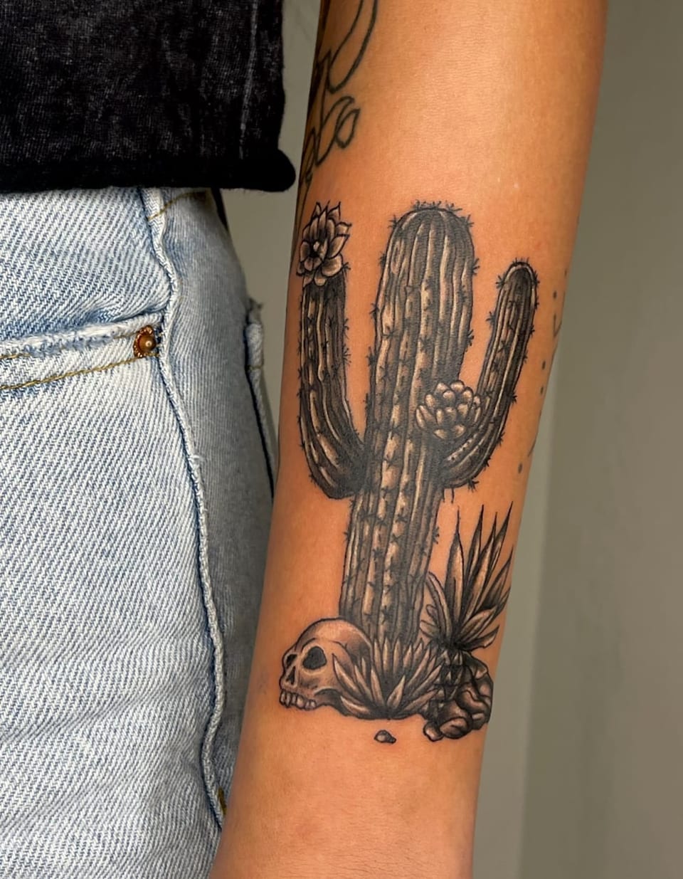 A black and grey illustrative flowering cactus, skull and desert plants run down an inner forearm.