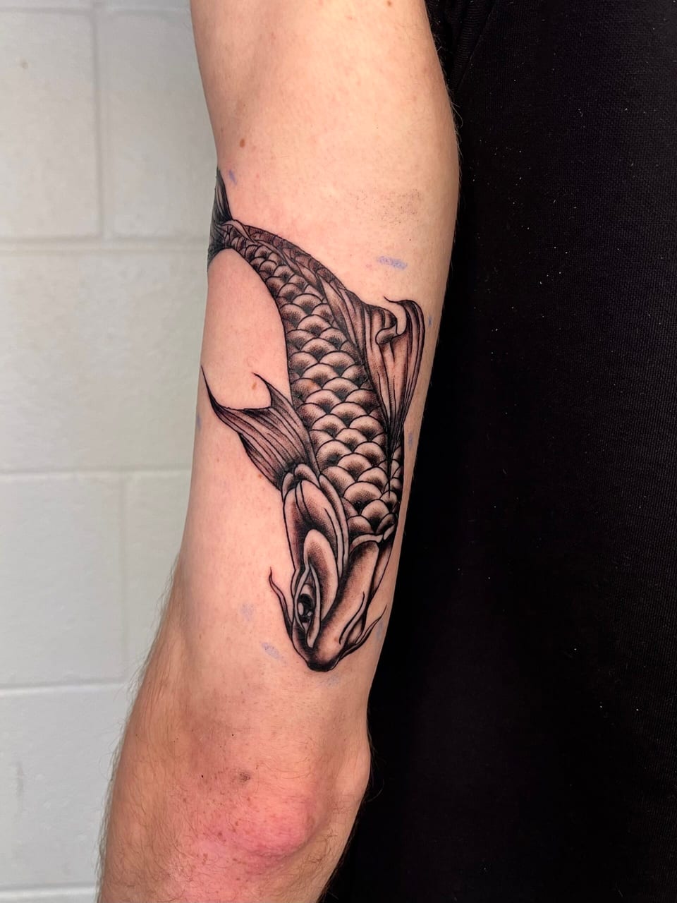 A black and grey Japanese-style koi with detailed scales swims head-down along an outer upper arm.