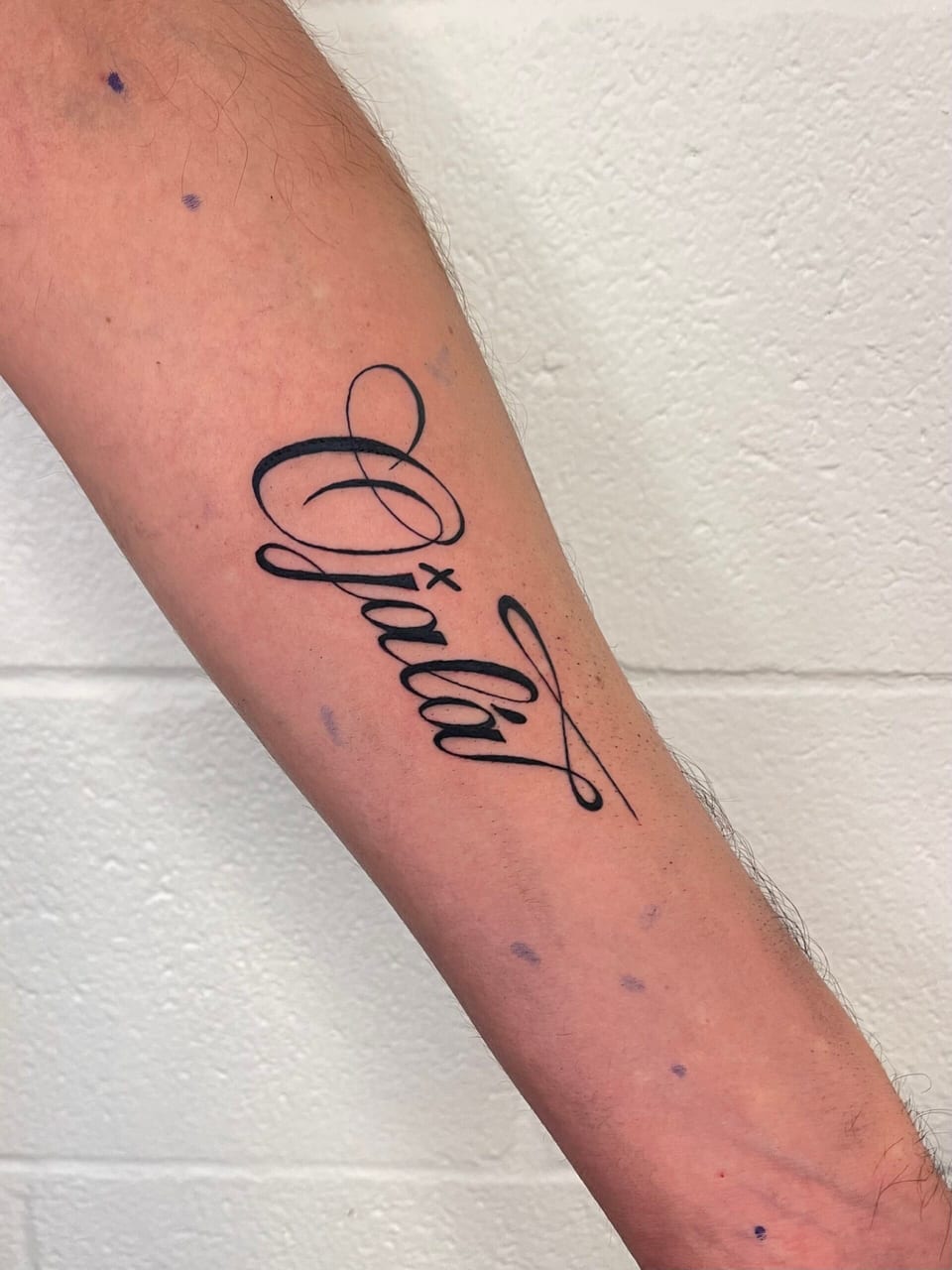 Black cursive lettering with long looping flourishes stretches diagonally across an inner forearm.