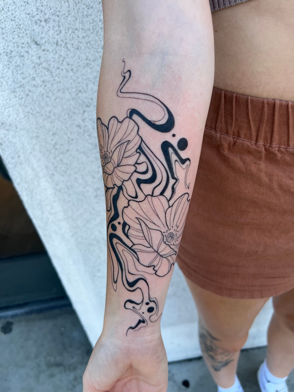 Fine-line flowers sit among flowing blackwork swirls and dots along an inner forearm.