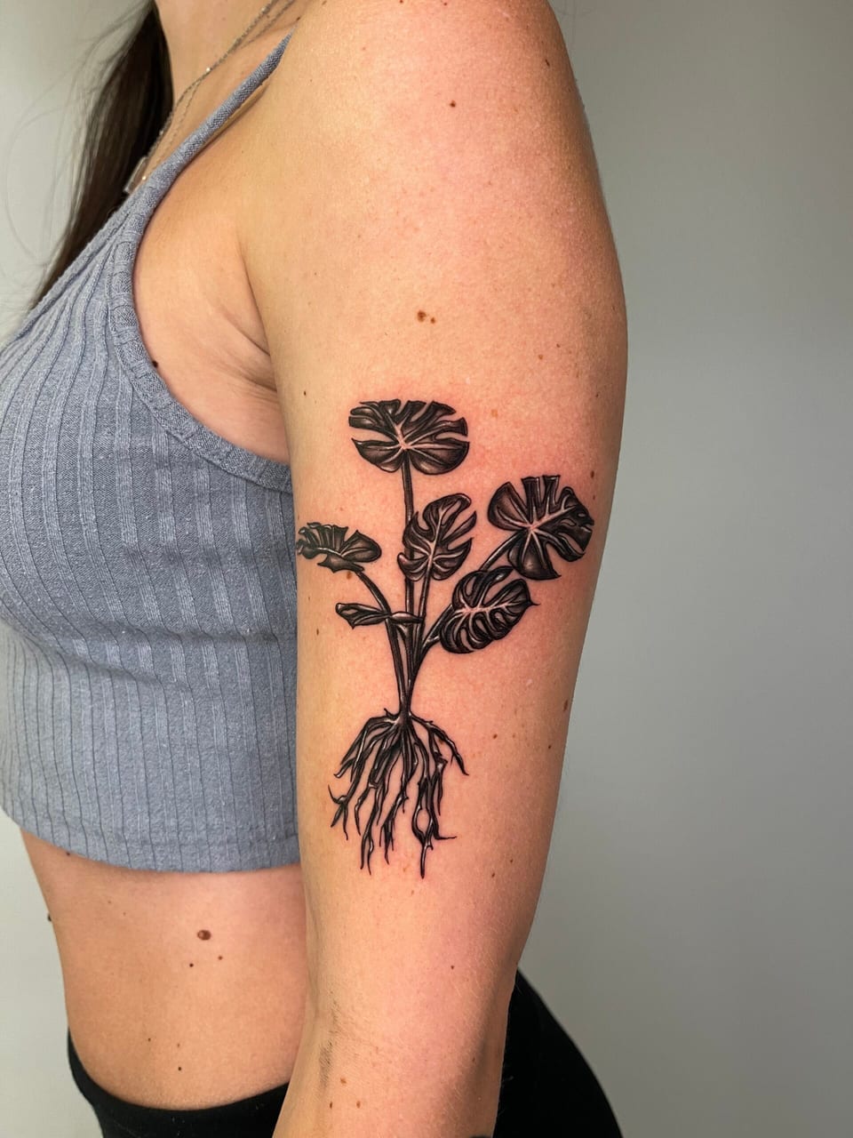 A black and grey illustrative monstera plant with exposed roots runs down an outer upper arm.