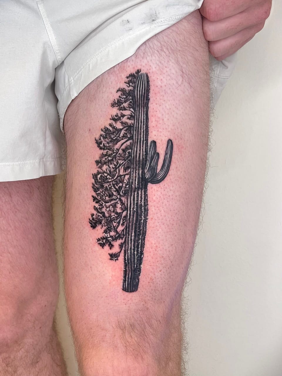 A black and grey illustrative cactus merges with leafy tree branches along a thigh.