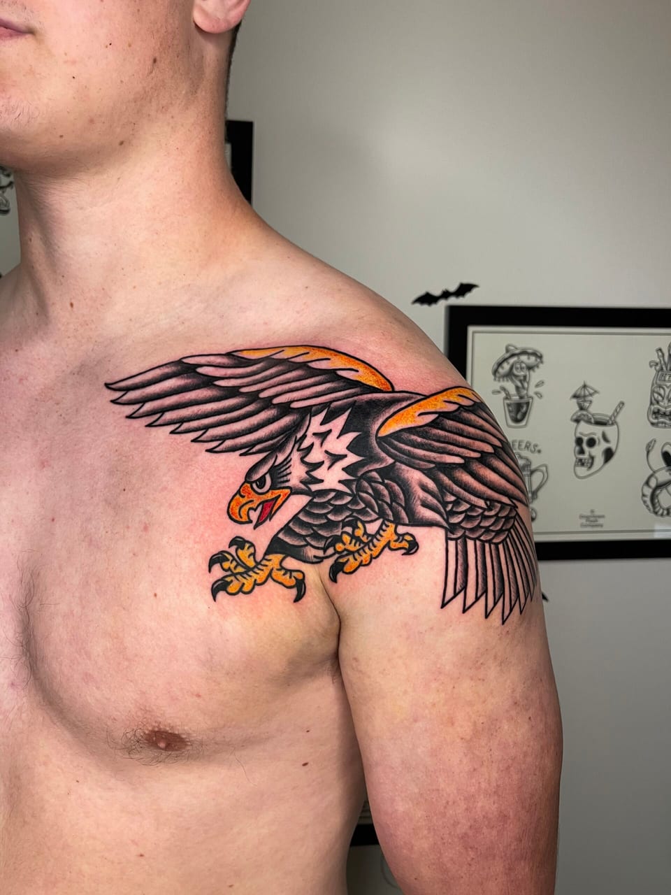 A black and orange traditional eagle spreads its wings across a shoulder and upper chest.