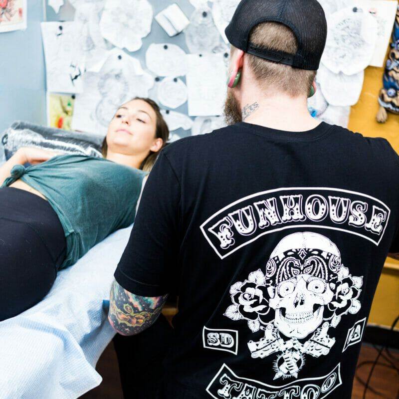 A man is undergoing the process of getting a custom tattoo on a woman's body.