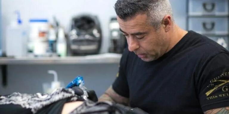 A man getting tattooed by Leo Cadenazzi in a tattoo shop.