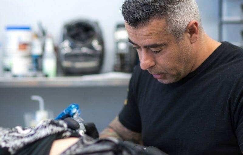 A man getting tattooed by Leo Cadenazzi in a tattoo shop.