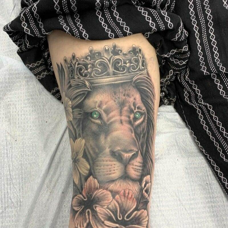 A tattoo of a lion with a crown and flowers.