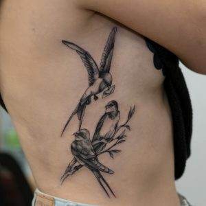 A black and white tattoo of two birds on a branch.