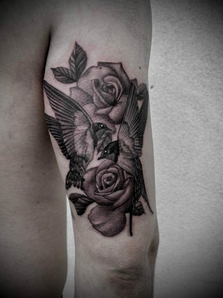 A black and grey tattoo of a hummingbird and roses.