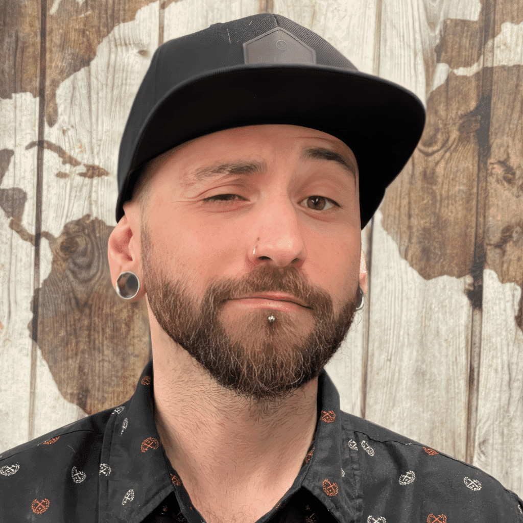 A man with piercings showcasing tattoos in front of a wooden wall.