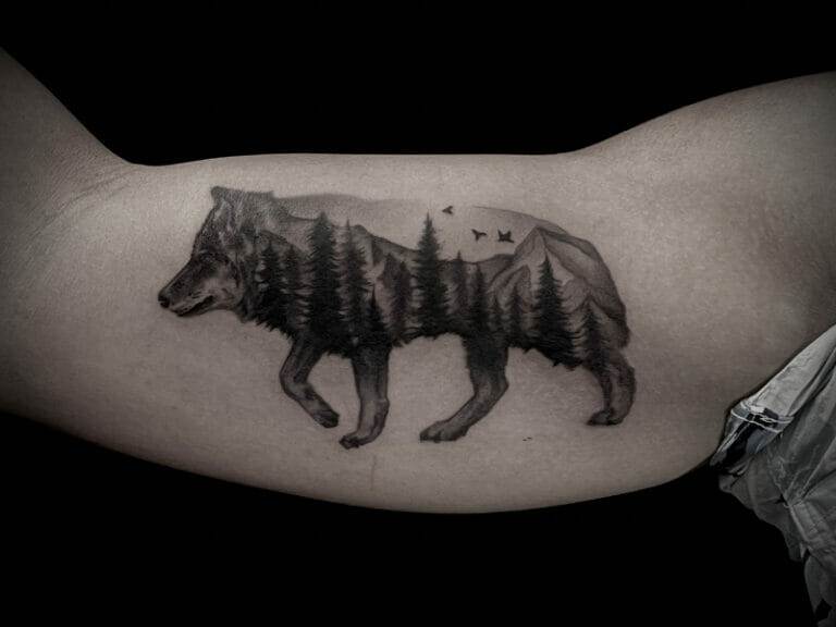 A black and white tattoo of a wolf in the mountains.