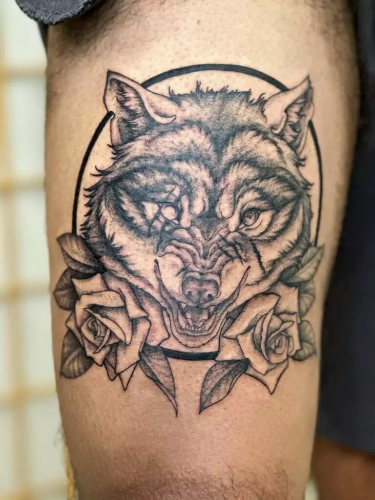 A tattoo of a wolf with roses on his thigh.
