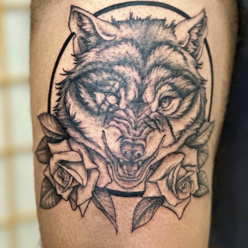 A tattoo of a wolf with roses on his thigh.