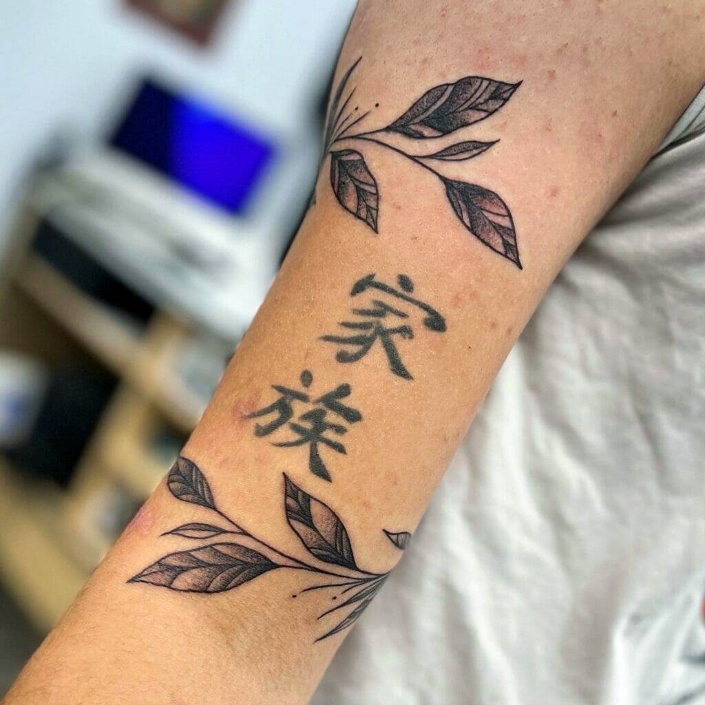 A tattoo with chinese characters and leaves on the arm.